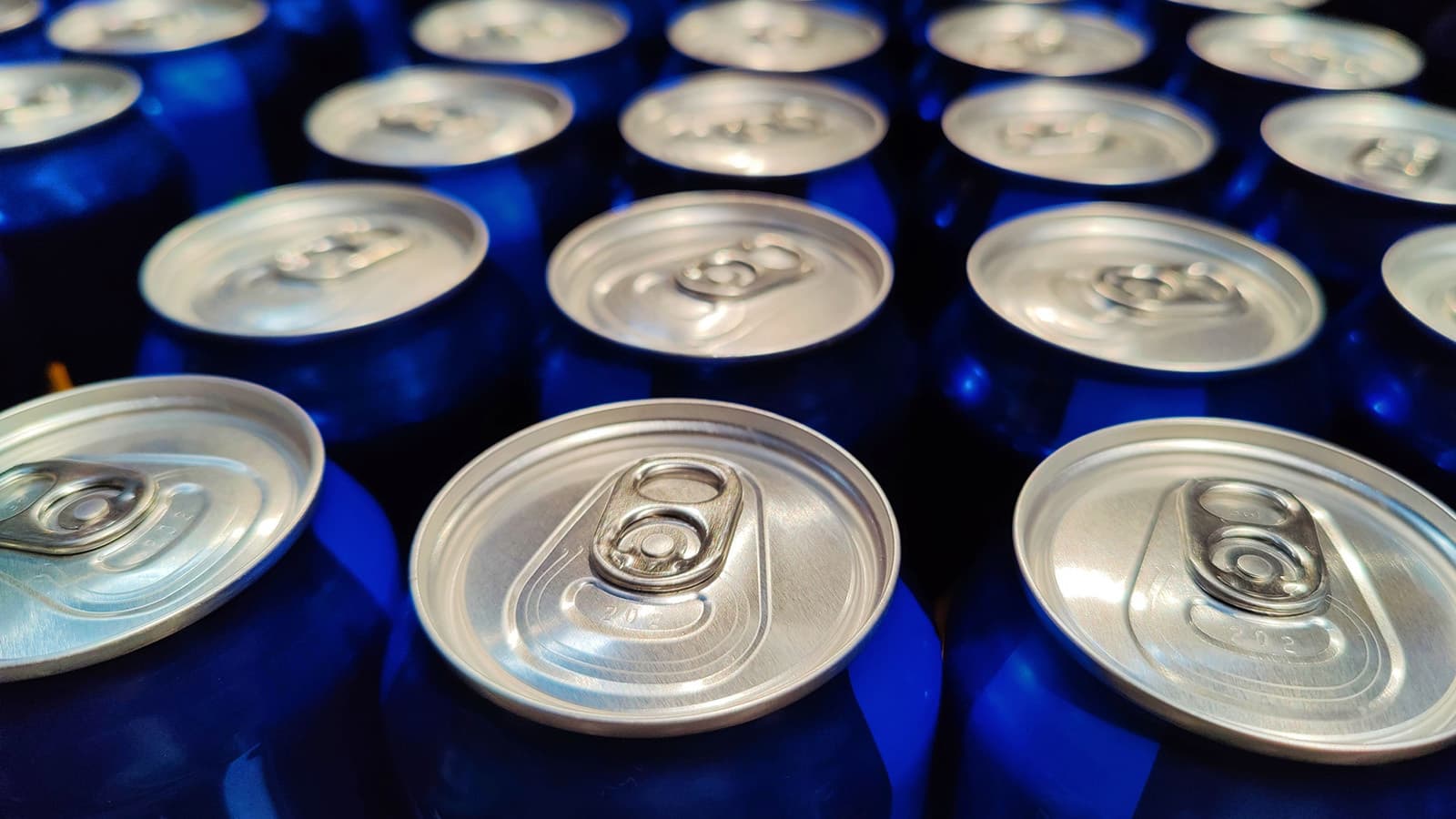 Blue soft drink cans with silver tops lined up in a factory.