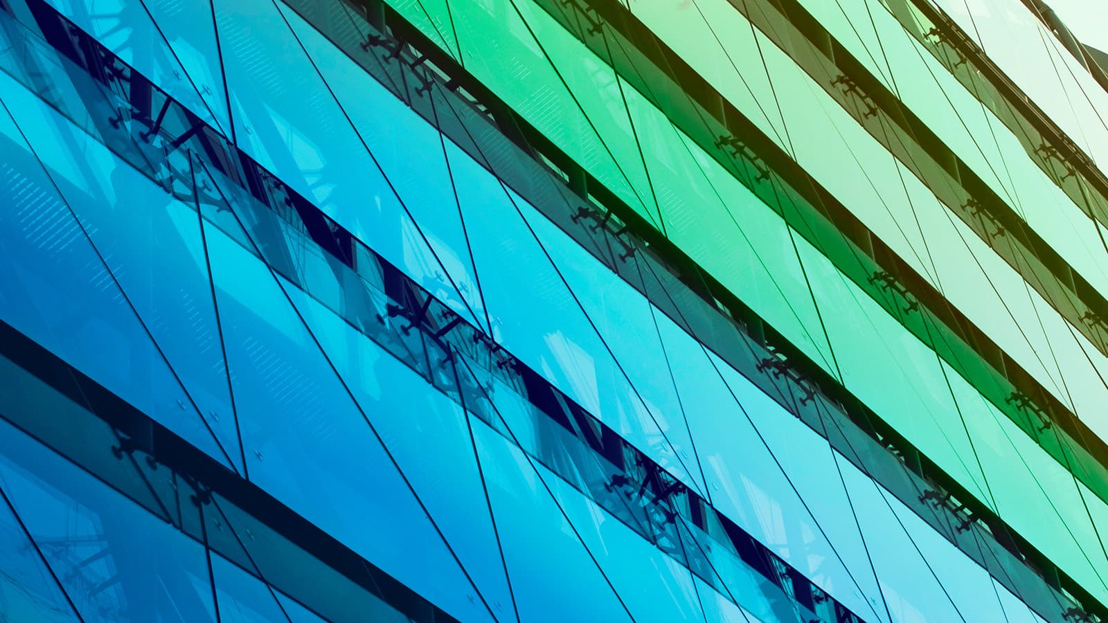 An abstract, angled photo of an office building's glass facade, fading from blue to green with diagonal and cross-sectional panels