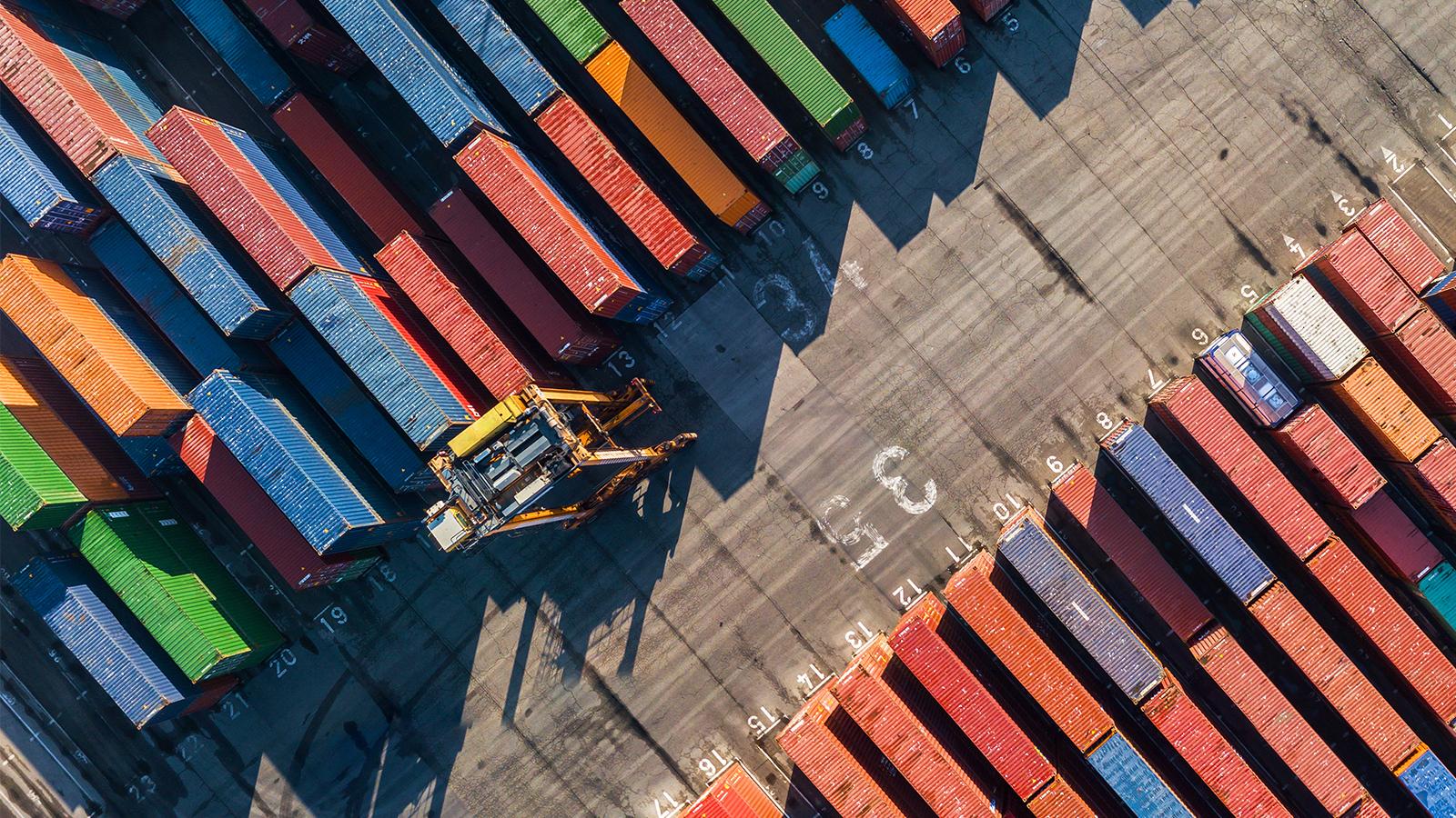 Aerial view of container port, just showing the dock with containers and a forklift.
