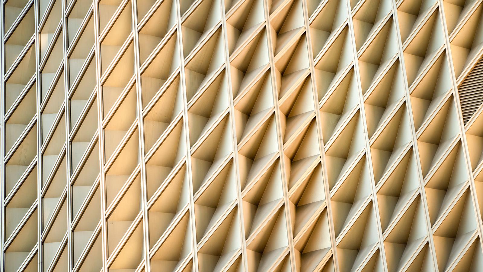 Cream-coloured building exterior with geometric detail, criss-crossing framework.