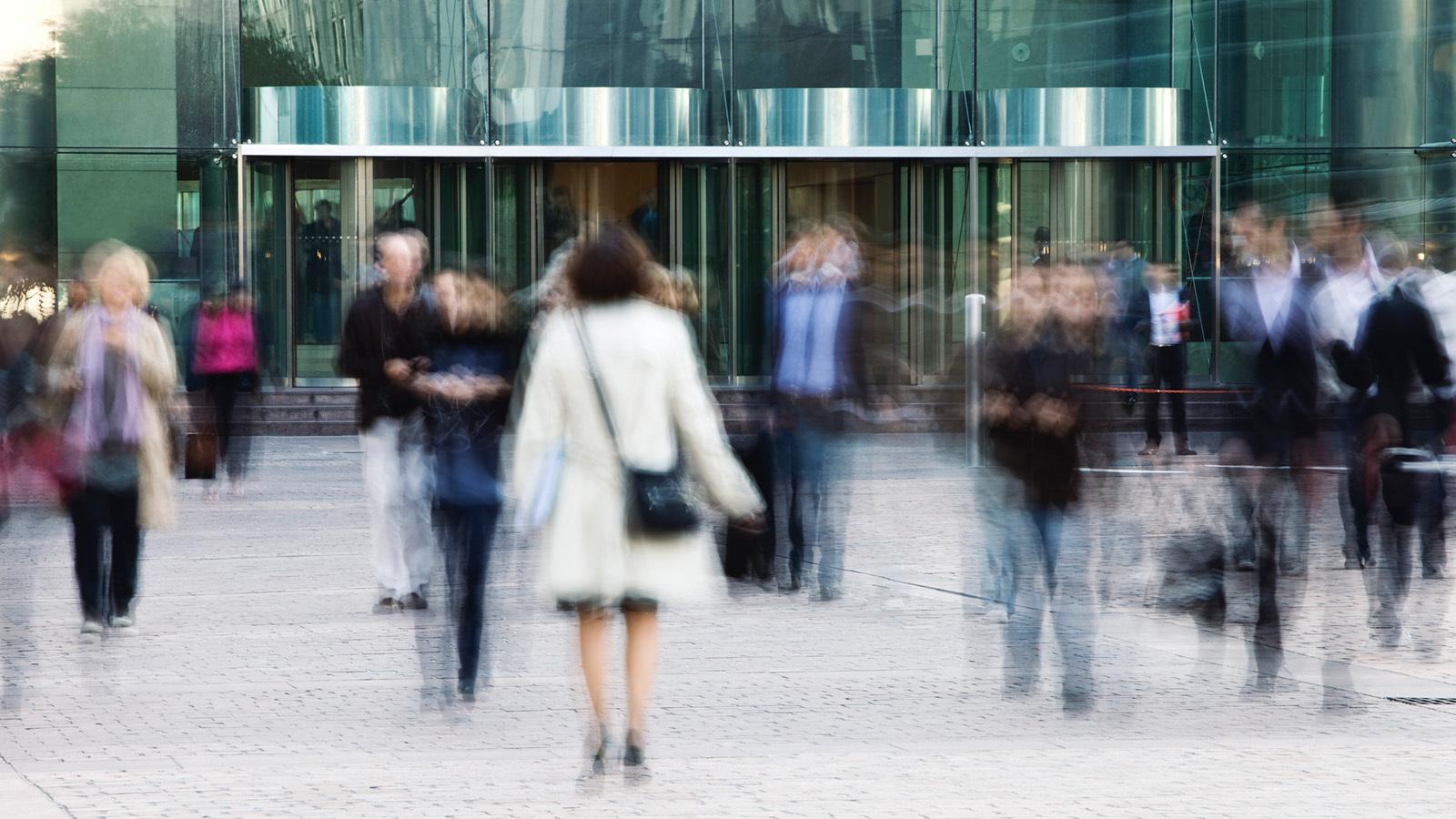 Business professionals entering and exiting an office building through revolving doors.