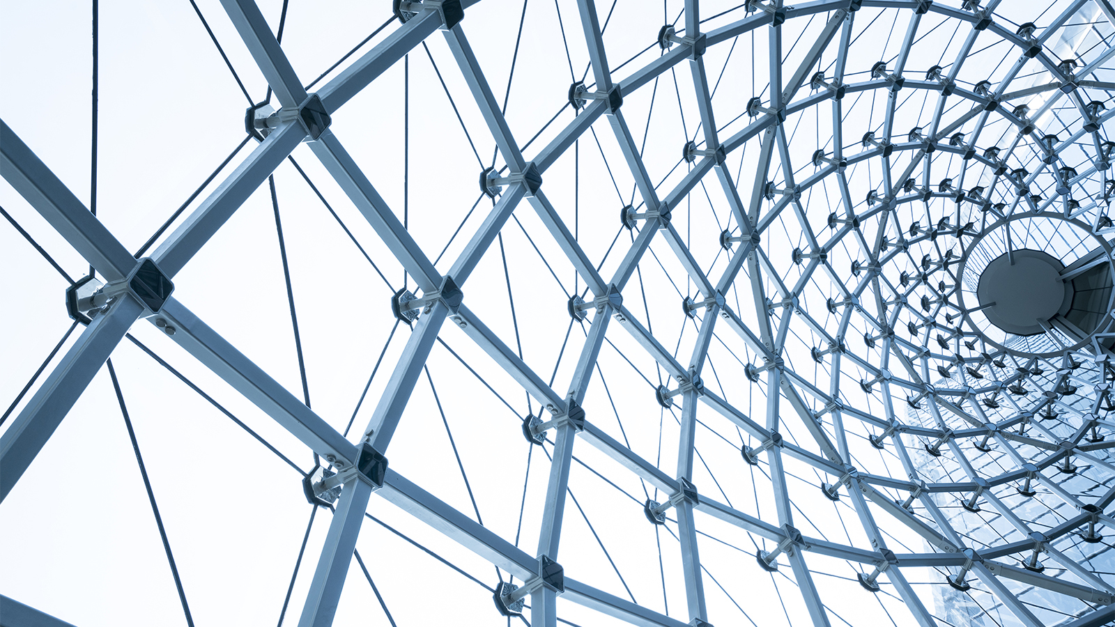 Close-up of a building with metal steel framework and glass, viewed from an interesting angle. Grey-blue framework with clear panels.