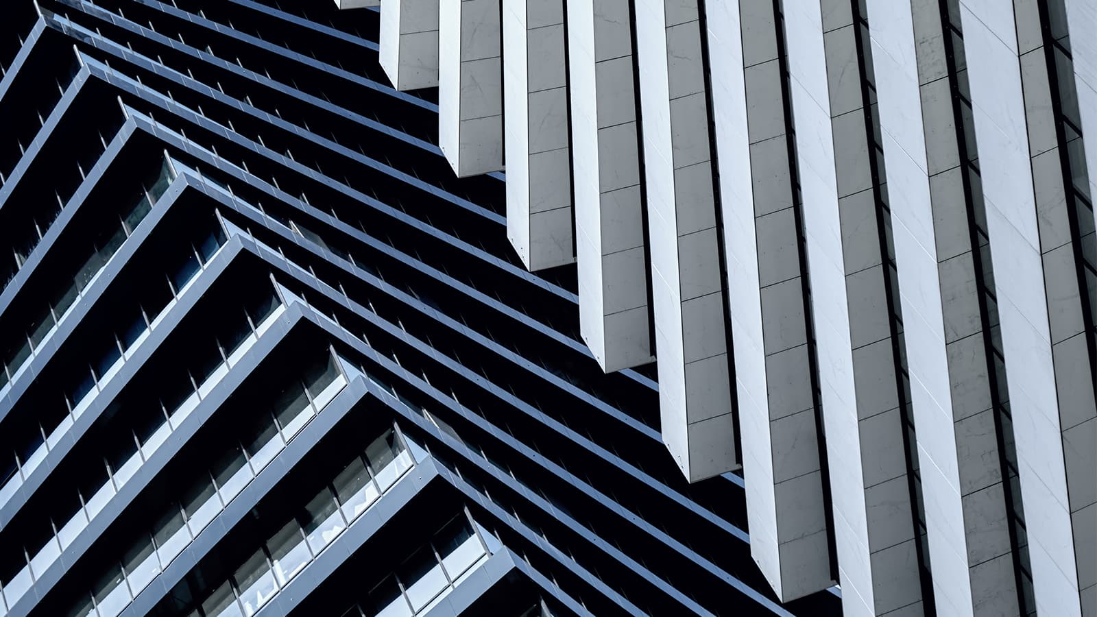 Two corporate buildings converging. Used here to represent the concept of a merger. The colours of one building are dark blue / black and the other white/grey.